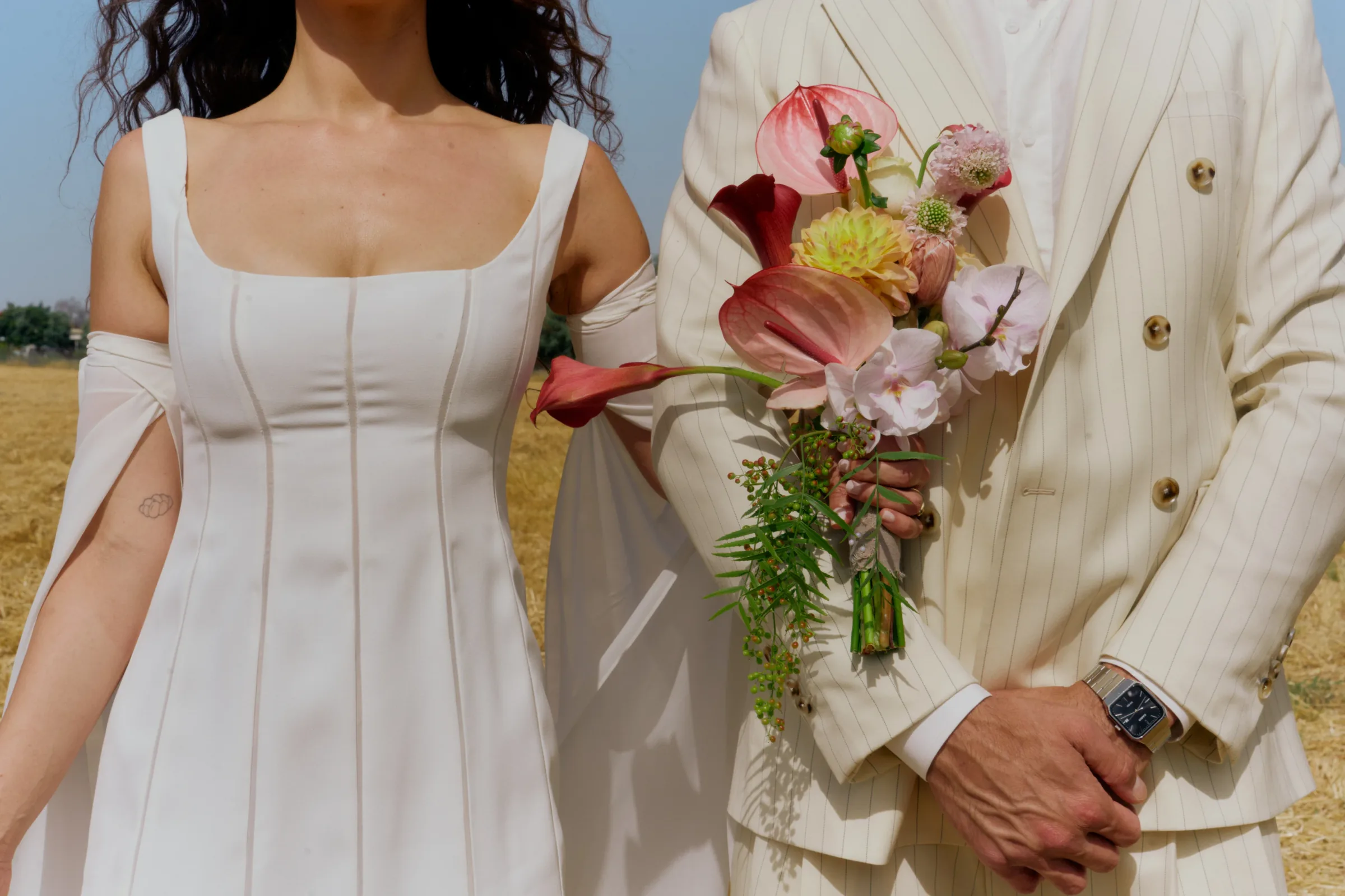 A bride and groom holding a bouquet in a summer field